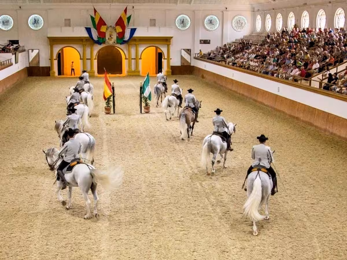 Elegant horse show with riders in traditional attire performing in a grand indoor arena before an audience.