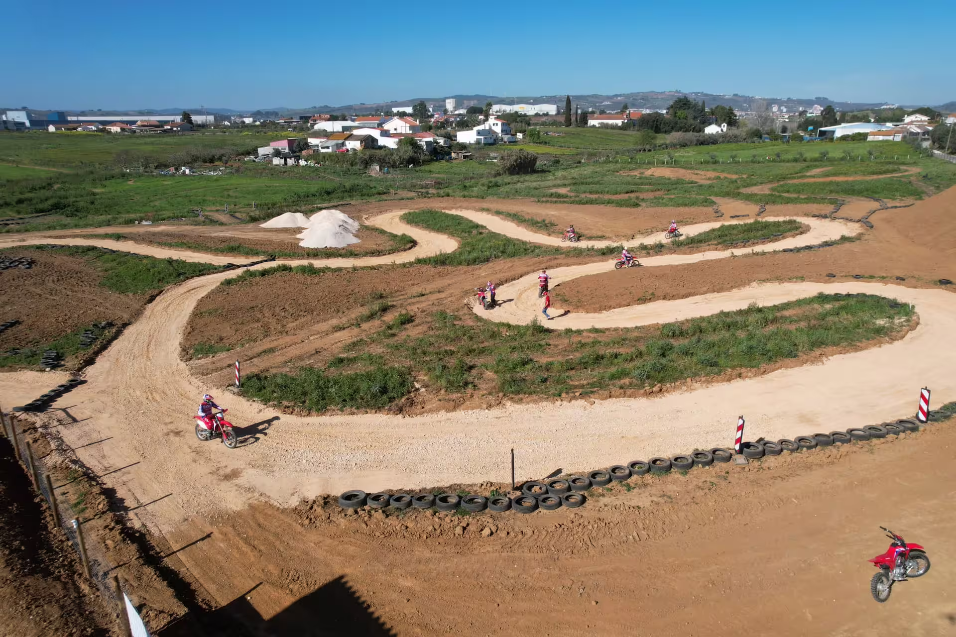Aerial view of winding dirt track with enduro riders navigating turns in scenic Carregado countryside.
