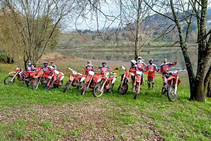 Enthusiastic riders with motorbikes gather by a picturesque riverside, enjoying the Marco de Canaveses enduro tour.