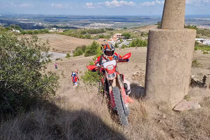 Enduro rider navigates rugged Lisbon hillside during small group adventure tour with scenic views.