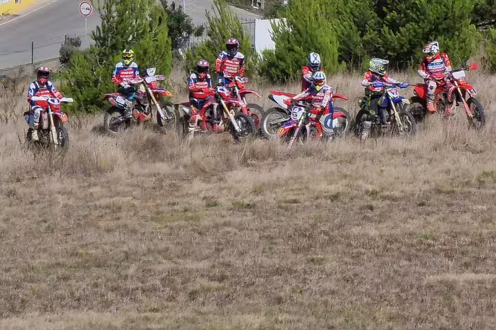 Group of enduro riders on dirt bikes pause in a grassy field, ready for an exciting Lisbon trail experience.