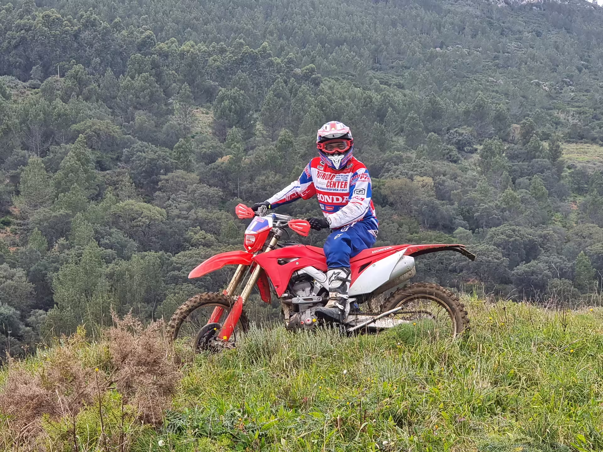 Rider on red dirt bike exploring lush green hills during 3-hour Enduro Tour in Carregado, Lisbon.