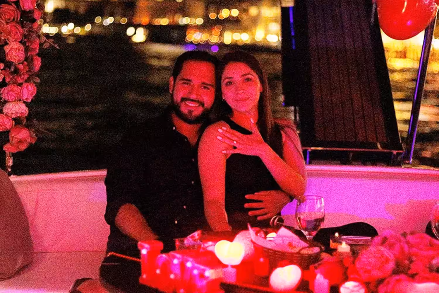 Engaged couple celebrating on a luxury yacht dinner cruise with candles, roses and city lights after proposal