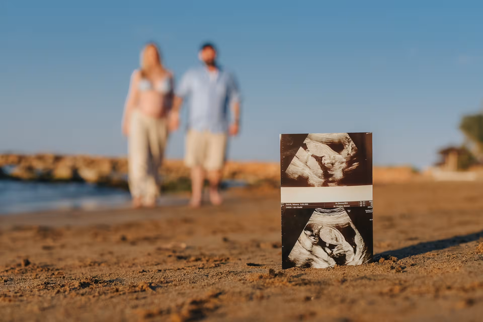 Couple at Heraklion Venetian Port holding an ultrasound photo on the beach, capturing a special engagement moment.