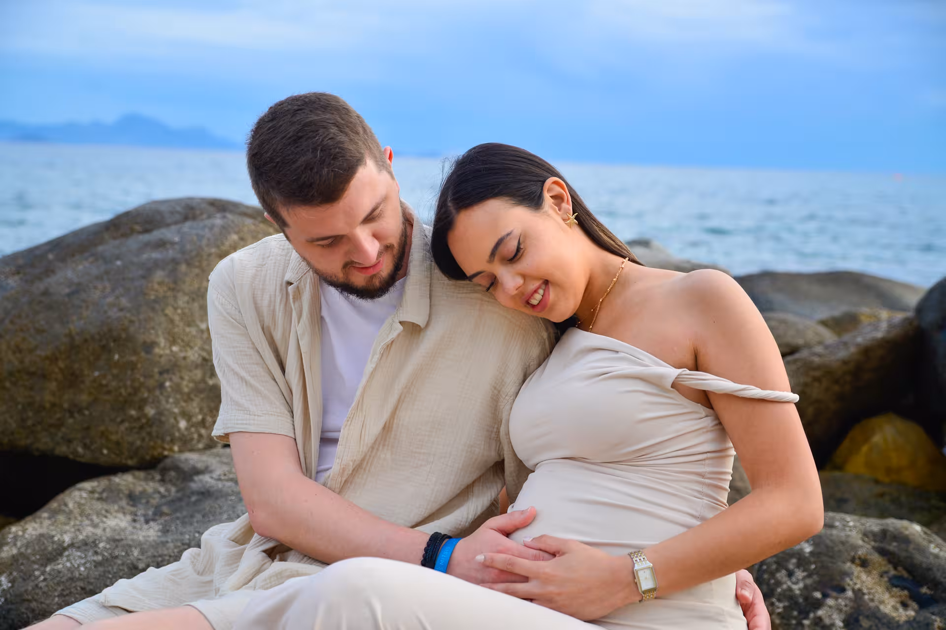 Couple embracing on rocky shore at Heraklion Venetian Port, perfect for engagement photoshoot with scenic sea backdrop.