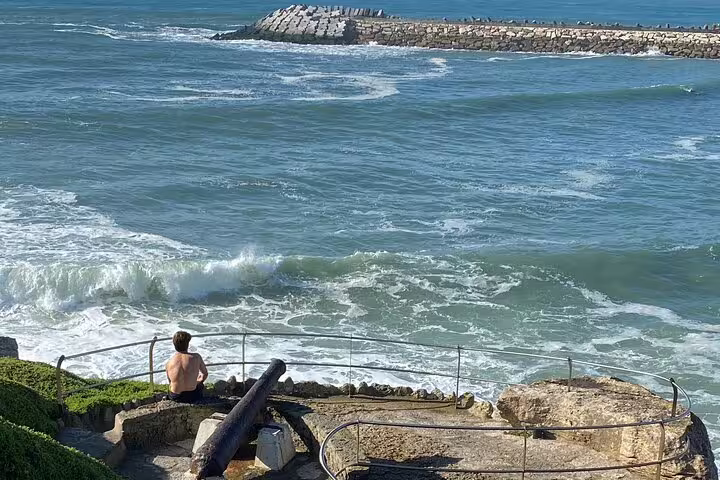 A person enjoys the serene ocean waves and rocky shoreline in Ericeira, a highlight on the Sintra tour itinerary.