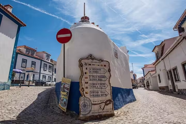 Charming street scene in Ericeira with traditional Portuguese architecture and directional sign, part of the Mafra, Ericeira & Queluz private tour.