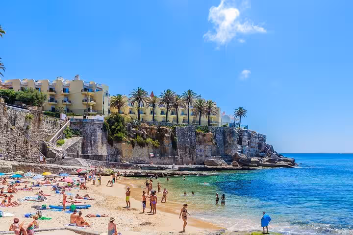 Sunny Estoril Beach with tourists enjoying the pristine waters and scenic views of cliffs and palm trees in Cascais.