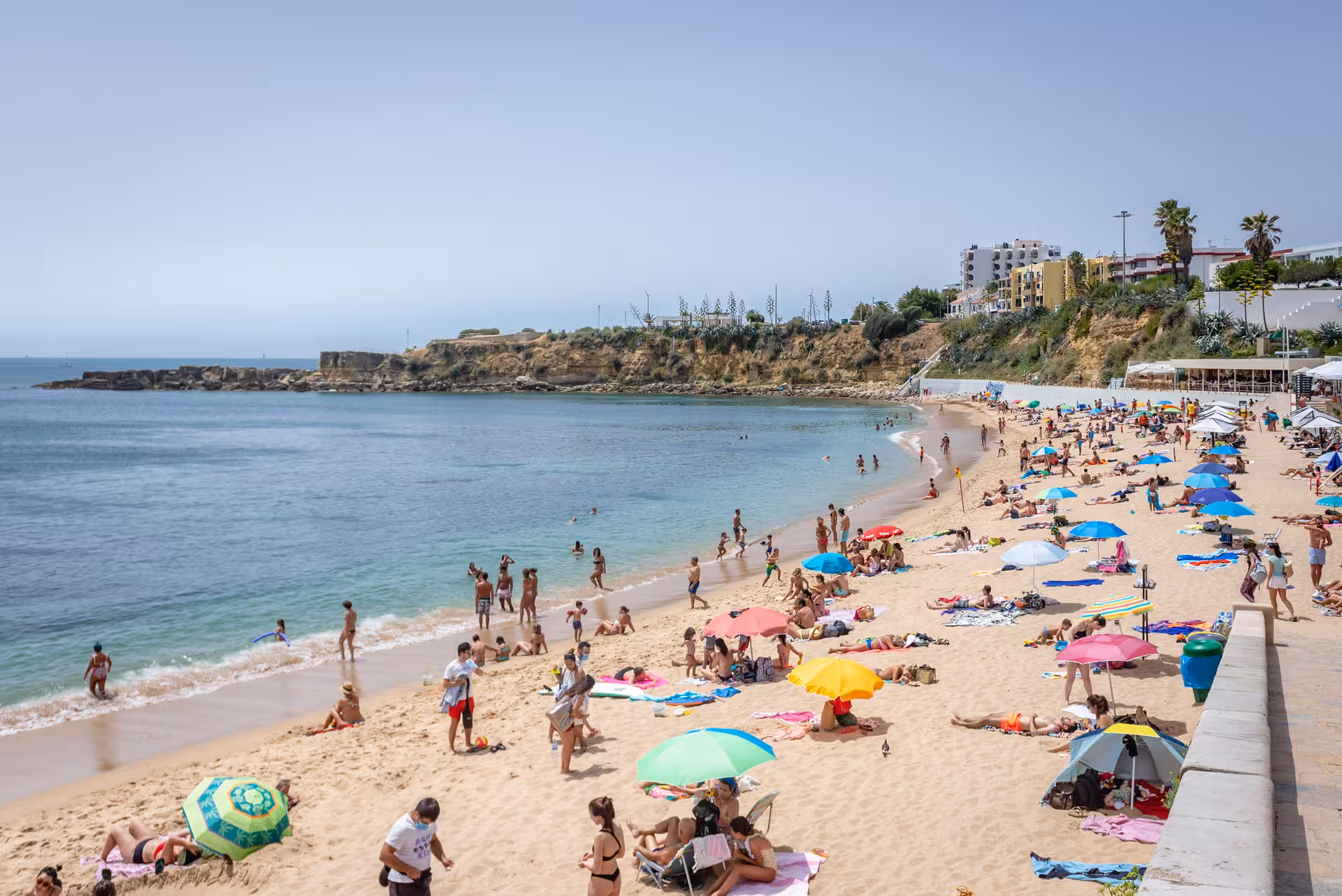 Sunny day at Estoril beach with colorful umbrellas and families relaxing, highlighting a fun Lisbon coastal getaway.