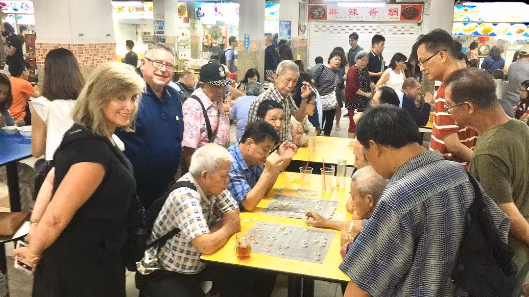 Group observing locals playing traditional board games in bustling food court.