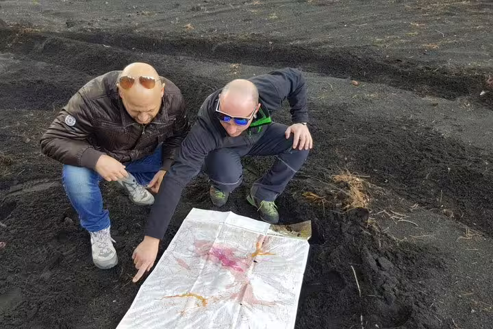 Guides review a volcanic map on Mount Etna lava fields during full-day Jeep tour from Taormina with lunch