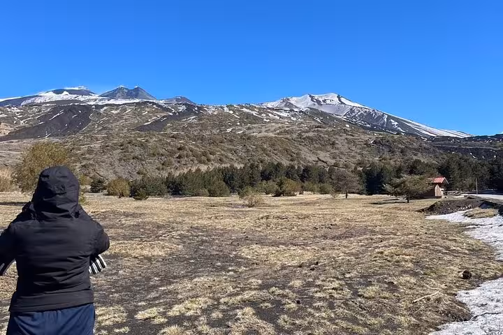 Traveler in winter gear admiring the snow-capped peaks of Mount Etna under a clear blue sky on a morning tour.