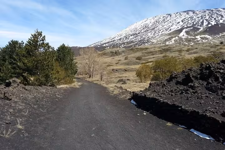 Scenic pathway with volcanic landscapes and snow-capped Mount Etna under a clear blue sky, ideal for morning tours.