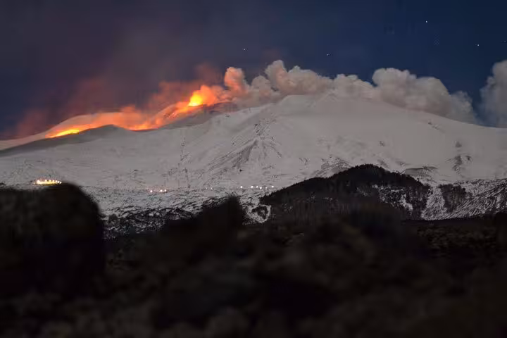 Lava and smoke illuminate Mount Etna under a starry night, showcasing natural beauty on the Etna Sunset Tour.