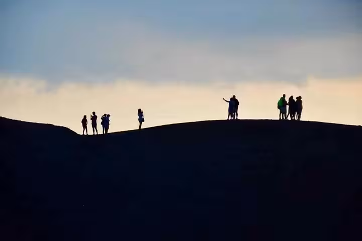 Silhouetted tourists explore the crest of Mount Etna at sunset, highlighting adventure and discovery on the tour.