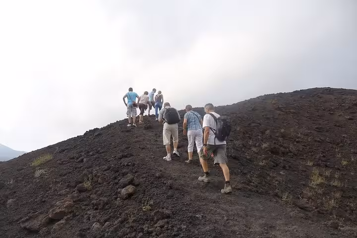 Tourists on an Etna trekking adventure, climbing the volcanic slopes with backpacks, highlighting an active group tour.