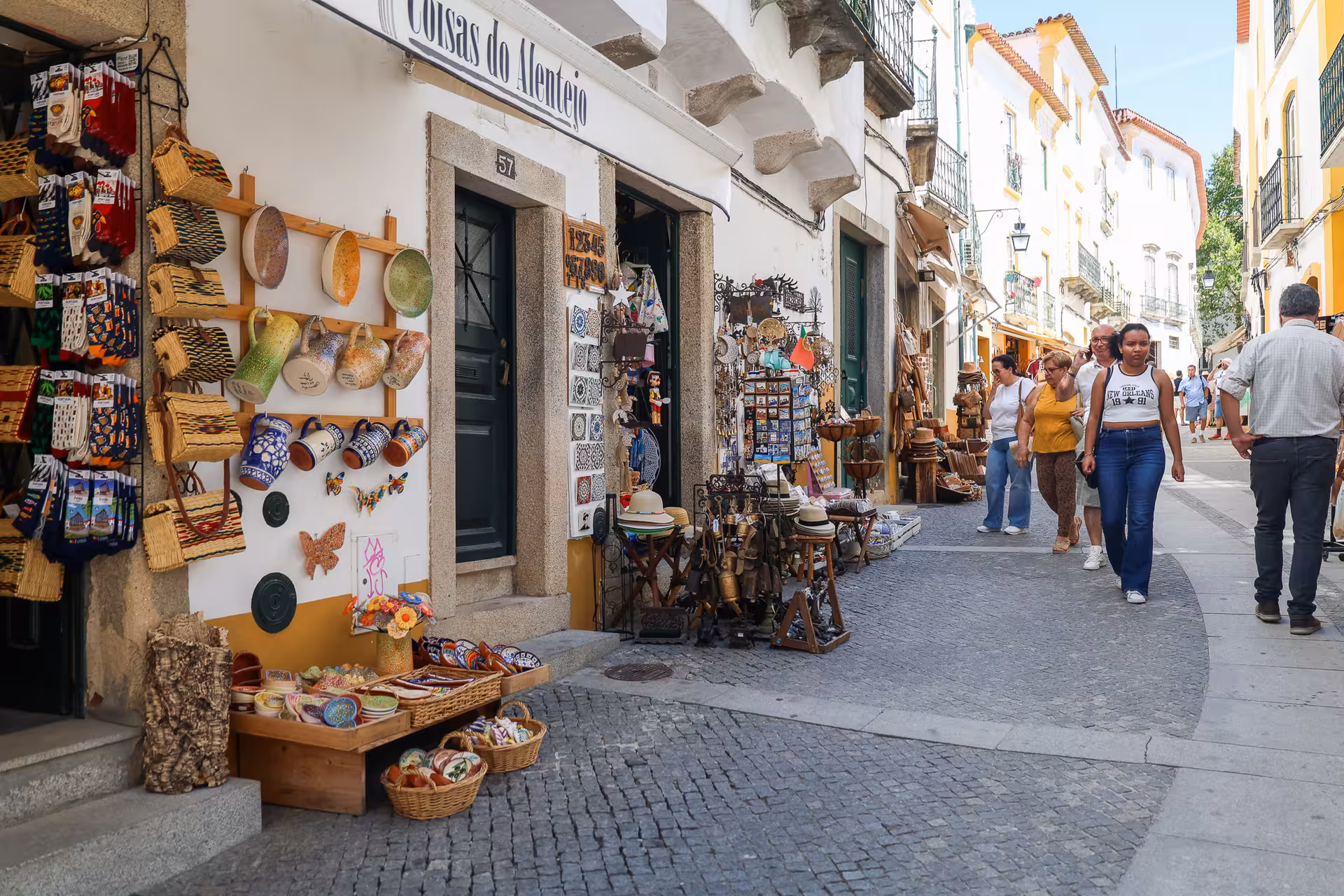 Tourists explore a charming Alentejo street with colorful local crafts and souvenirs on the Évora Wine Tour.