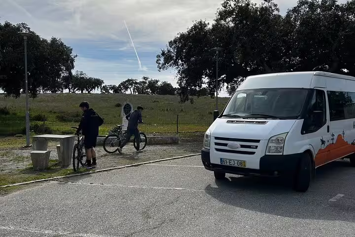 Cyclists preparing for a bike tour near a parked van in a serene countryside setting outside Évora.