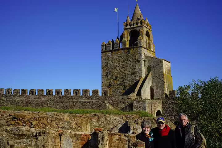 Tourists enjoying a sunny day exploring the historic castle in Évora, Portugal, with its ancient stone walls and a clear blue sky.