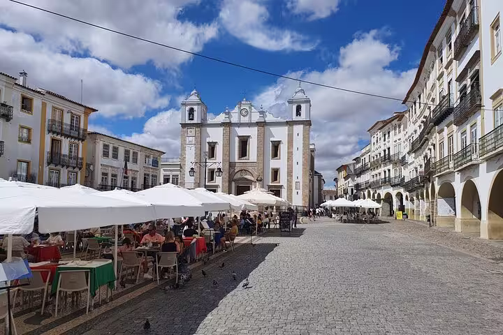 Charming cobblestone plaza in Évora with outdoor cafes, historic architecture, and blue skies on a small-group tour from Lisboa.