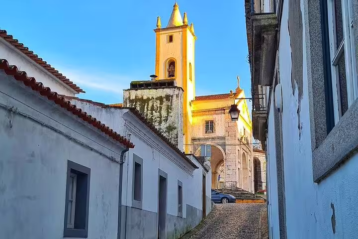 Charming narrow street in Évora with historic architecture and a bell tower, captured on a sunny day during a Lisbon day tour.