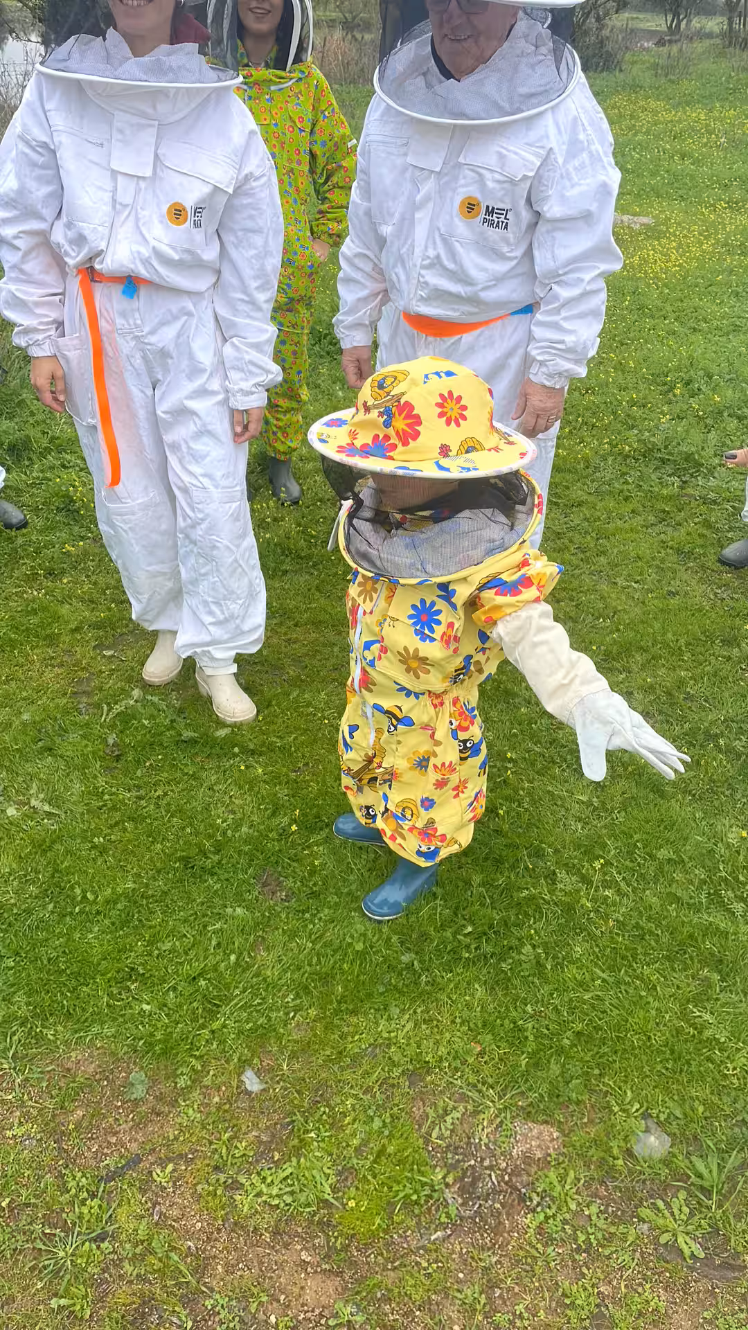 Visitors in colorful beekeeping suits explore a lush green field during the Évora honey tour.