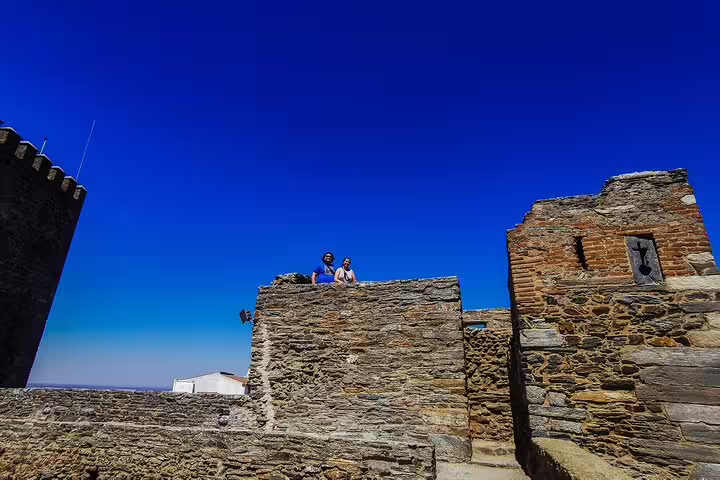 Tourists explore ancient stone walls under a clear blue sky on a day trip from Lisbon to Évora and Monsaraz.