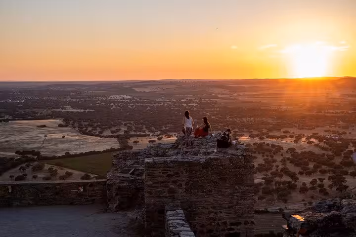 Travelers enjoying a sunset view over the vast landscape from Monsaraz Castle, highlighting the Évora tour experience.