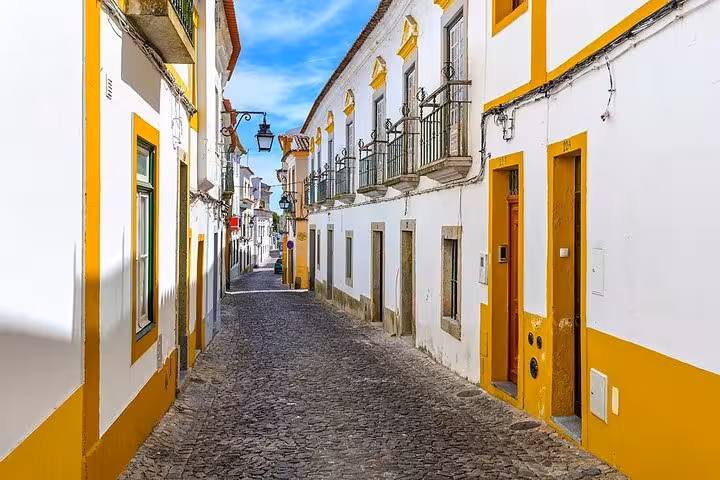 Charming street in Évora showcasing traditional whitewashed buildings with yellow trim under a clear blue sky.
