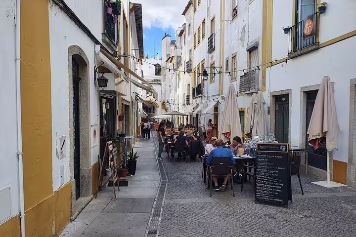 Tourists enjoy outdoor dining on a charming, narrow street in Évora, showcasing the historic ambiance of this Portuguese city.