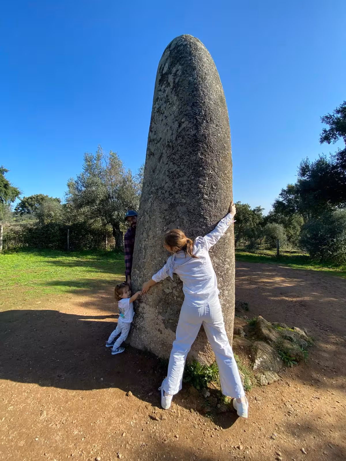 Visitors embrace a large standing stone at a prehistoric site in Évora, highlighting ancient history on a cultural tour.