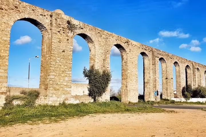 Historic Roman aqueduct in Évora, Portugal, showcasing ancient stone arches against a bright blue sky.