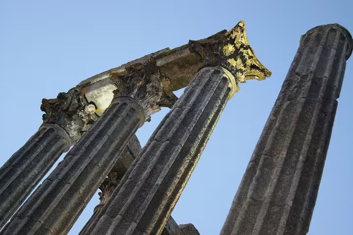 Ancient Roman temple columns under a clear blue sky in Évora, showcasing classical architecture on a day tour from Lisbon.
