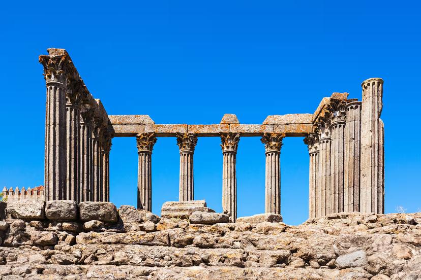 Ancient Roman temple ruins with tall stone columns stand against a clear blue sky in Évora, Portugal.