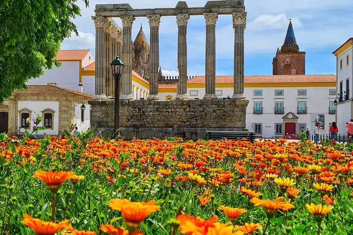 Vibrant orange flowers bloom in front of the ancient Roman Temple of Évora, a highlight of the full-day tour from Lisbon.