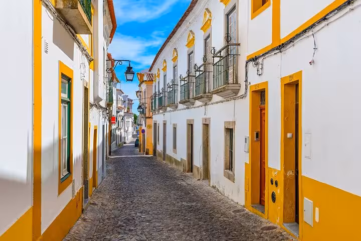 Charming narrow street in Évora with traditional white and yellow buildings, perfect for a cultural walking tour.