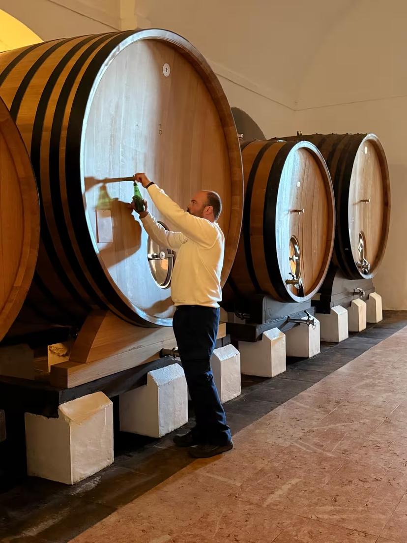 Winemaker samples wine from large oak barrel in historic cellar during Évora's exclusive wine tour.