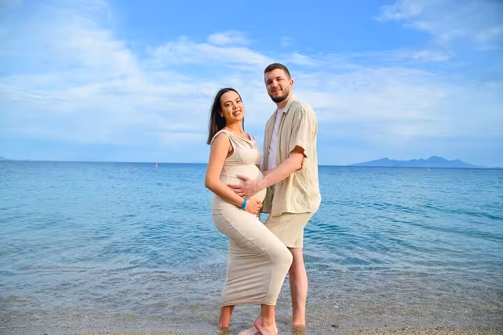 Expecting couple posing by the sea under a clear blue sky in Analipsi.