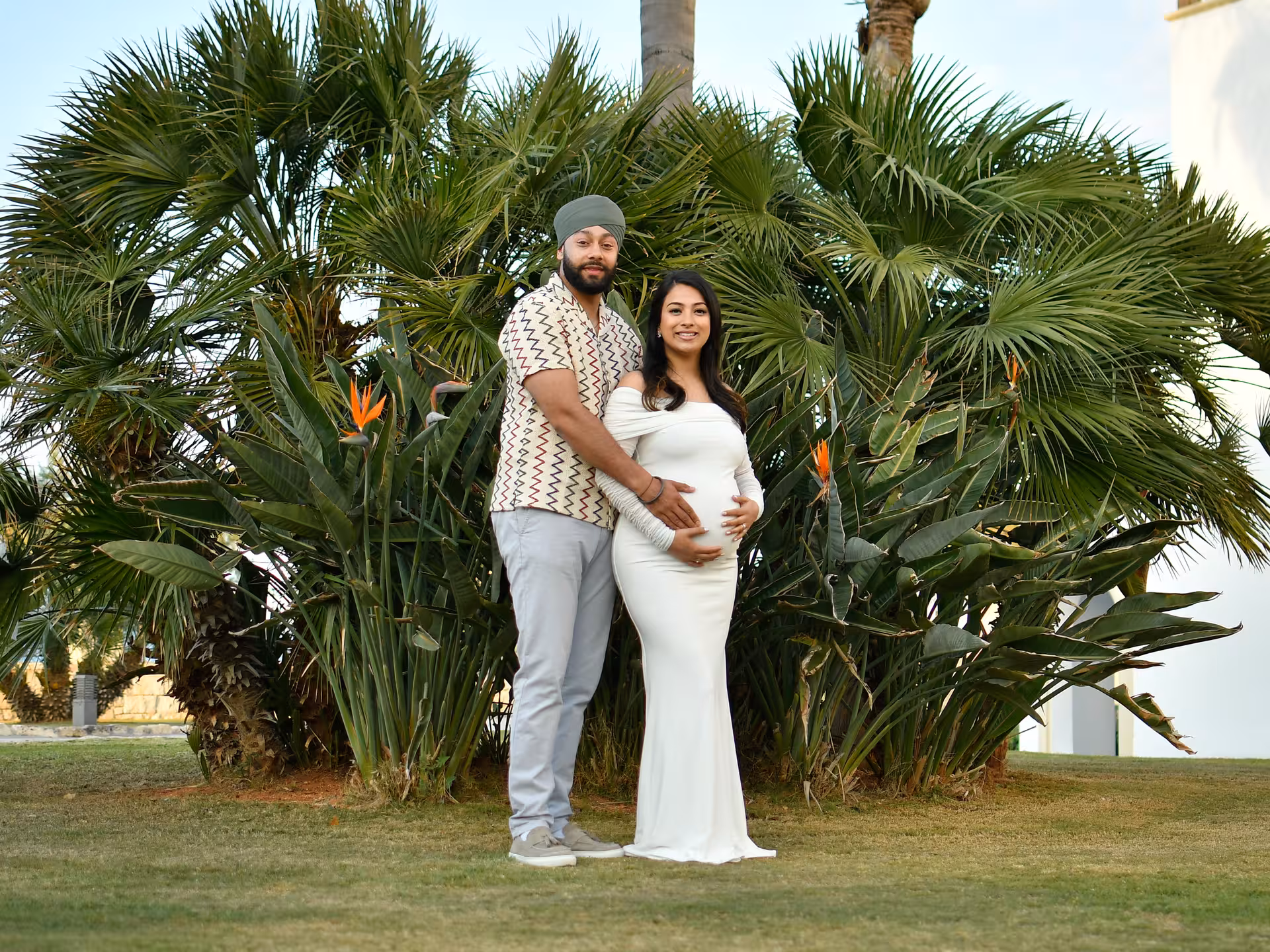 Expecting couple poses by lush palms during private Heraklion photoshoot, capturing special moments in nature.