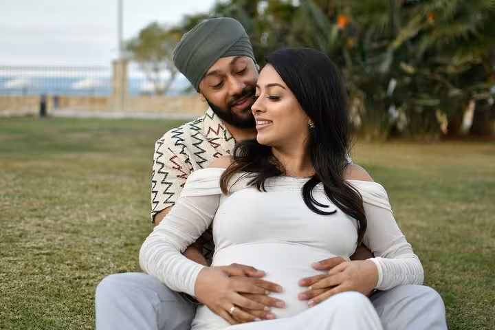 Expecting couple enjoying a serene moment on a sunny lawn in Ammoudara during a private photoshoot experience.