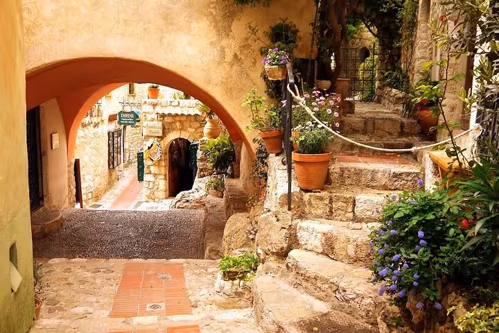 Charming cobblestone path and archway in Eze village adorned with vibrant flowers, highlighting Provence's allure.