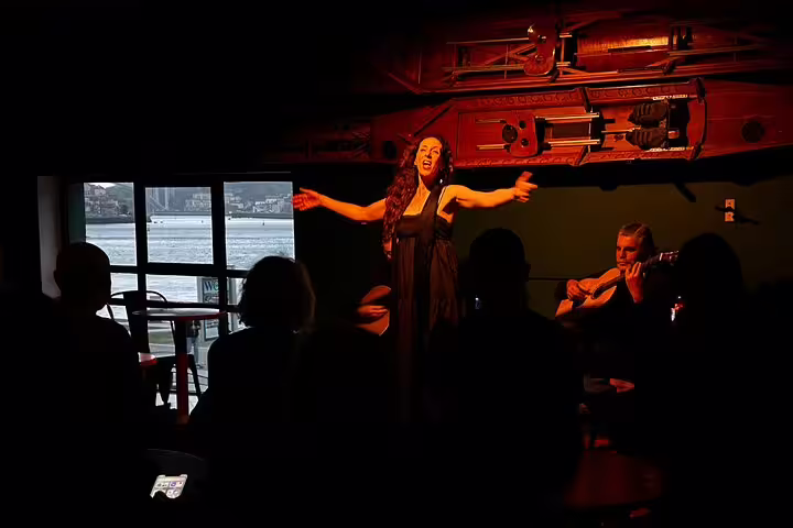 Fado performance by the riverfront in Porto, featuring a passionate singer and guitarist in an intimate, dimly lit venue.
