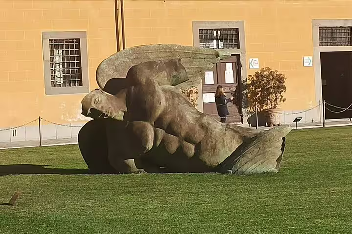 Modern fallen angel statue on lawn near Piazza dei Miracoli in Pisa, visited on Florence and Pisa tour from La Spezia