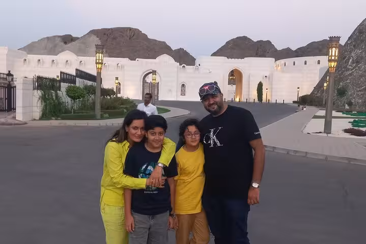 Happy family enjoying evening stop at Al Alam Palace area on a guided half-day Muscat City tour with mountain backdrop