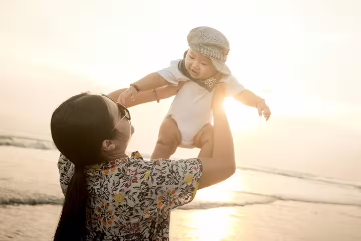 Family beach photo shoot in Bali at golden hour, mom lifting baby during private vacation photographer session