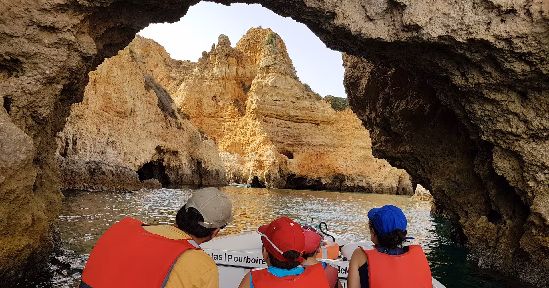 Family on a coastal boat tour at Ponta da Piedade, Lagos, admiring golden Algarve cliffs from a sea cave arch