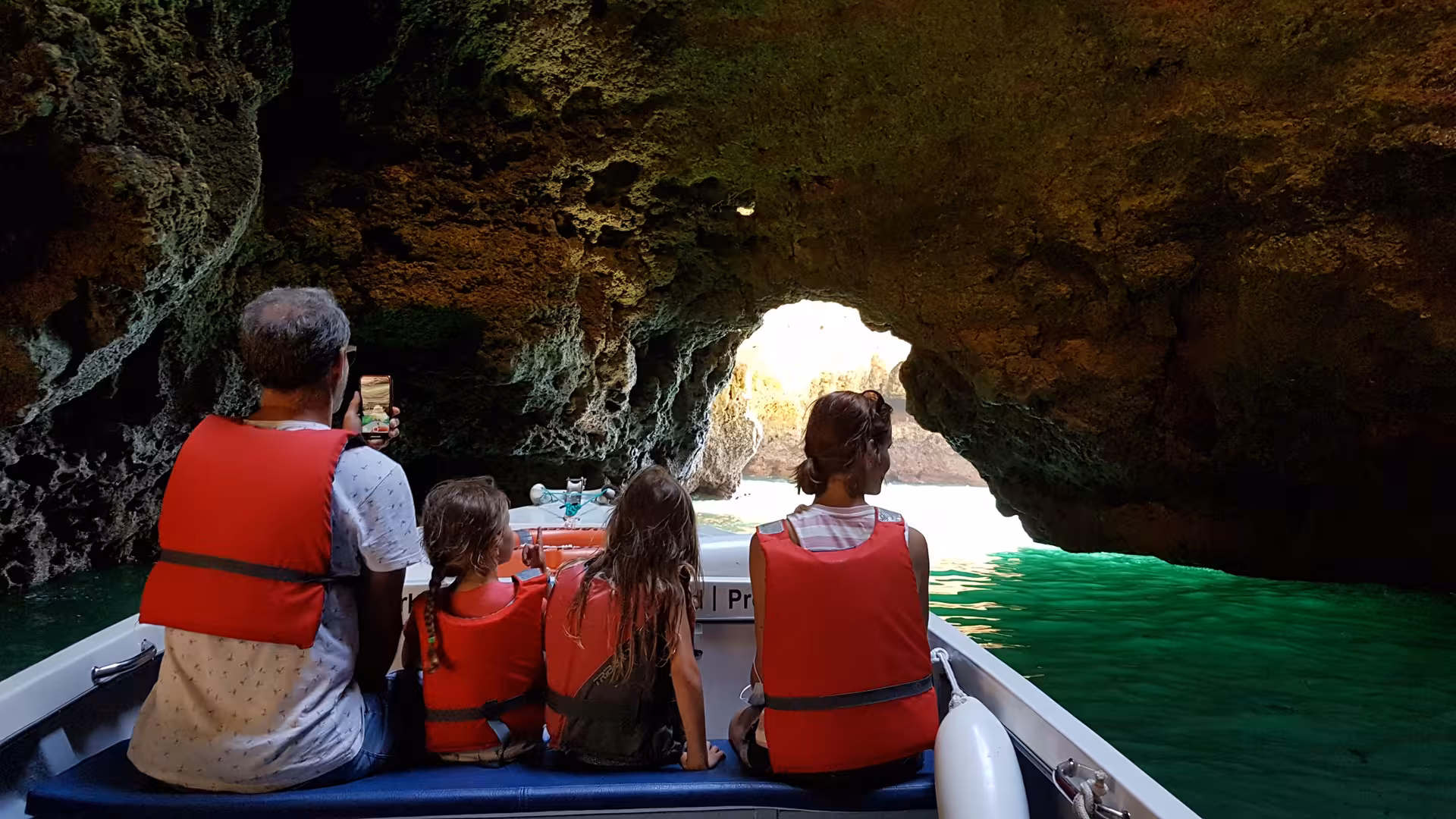 Family in red life jackets on a guided boat tour exploring a sunlit sea cave at Ponta da Piedade, Lagos Algarve