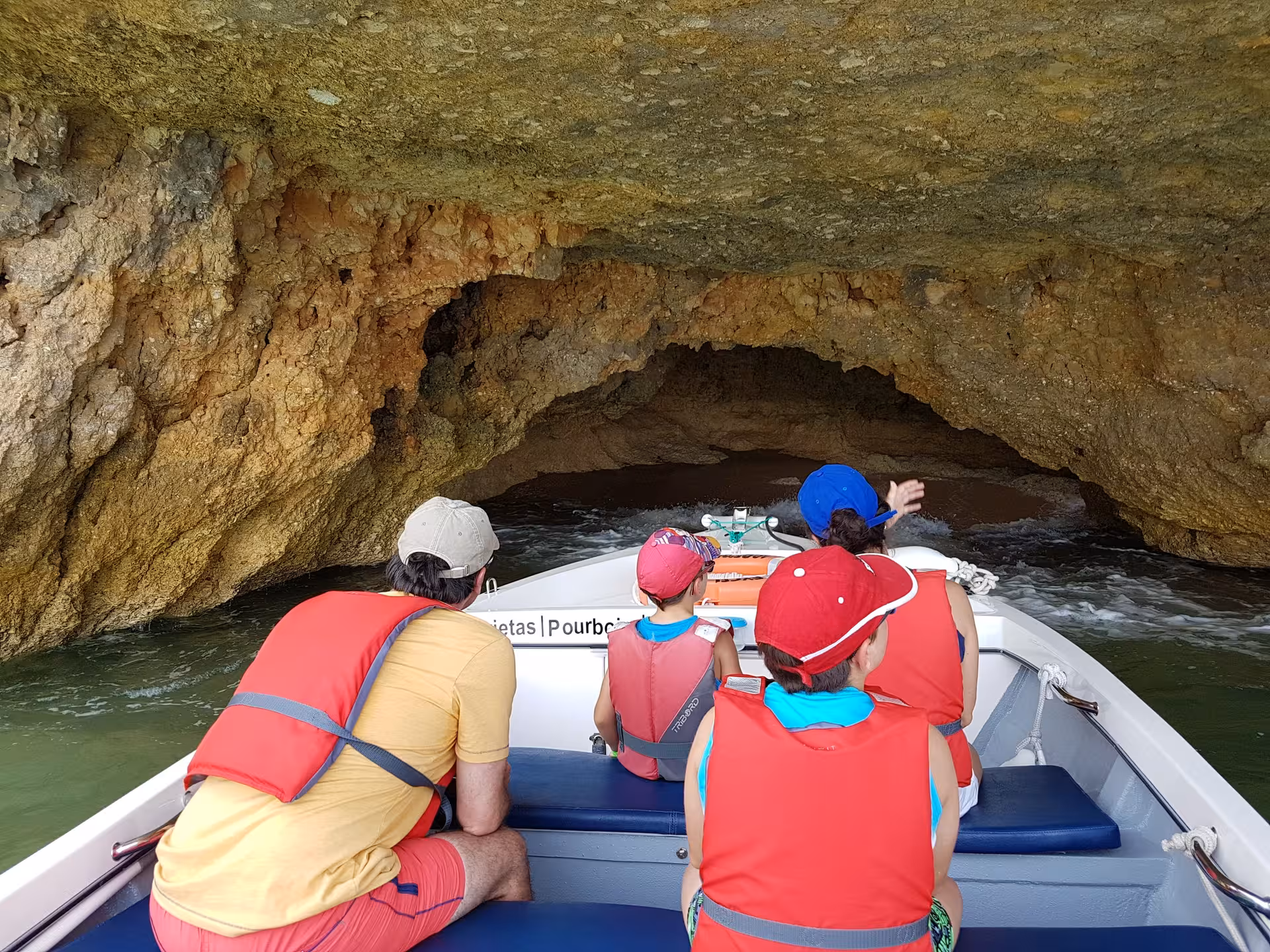 Family in life jackets on a Lagos boat tour glides into the rocky Ponta da Piedade sea caves along the Algarve coast