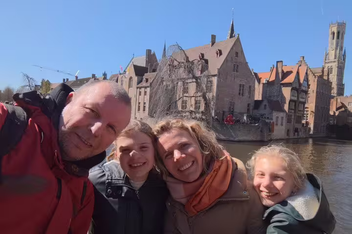 Family selfie by Bruges canal with medieval buildings, ideal for an e-scavenger hunt city exploration tour
