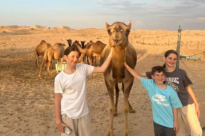 Family posing with camel in Ras Al Khaimah desert safari, camel ride stop before BBQ dinner camp